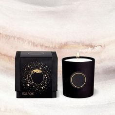 a black candle sitting next to a box on top of a white surface with gold foil