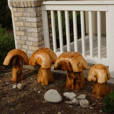 three wooden mushrooms sitting on the ground next to some rocks and flowers in front of a house