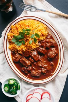 a white plate topped with meat and rice next to a bowl of green peppers on top of a table