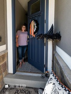 a woman standing in front of a blue door with halloween decorations on the side walk