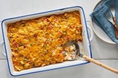 a casserole dish with meat and vegetables in it on a white table next to silverware