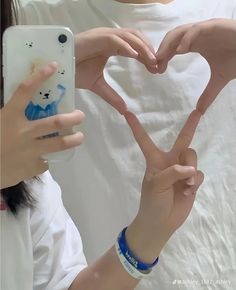 two people making a heart shape with their hands while one person takes a selfie