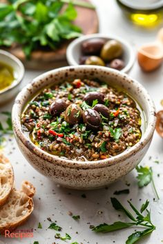 a bowl filled with olives and bread on top of a white table next to other bowls