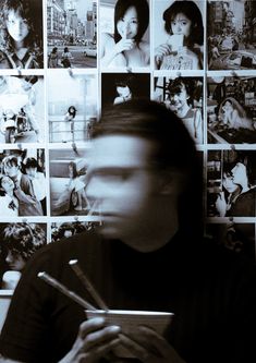 a man sitting in front of a wall covered with pictures and writing on a pen