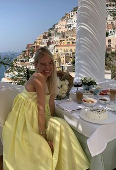 a woman in a yellow dress sitting at a table with a cake and flowers on it