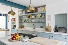 a kitchen with blue cabinets and white counter tops, gold pendant lights over the sink