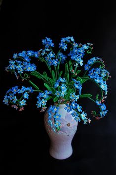 a white vase filled with blue flowers on top of a black table next to a wall