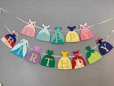 a happy birthday banner with princess dresses hanging from it's clothesline on the wall