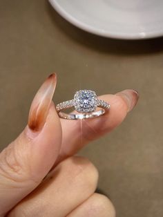 a woman's hand holding a ring with a diamond on it and the middle finger