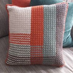 two pillows sitting on top of a couch next to each other, one with an orange and gray crochet pattern