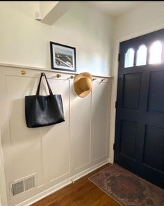 there is a hat hanging on the wall next to a black door and a purse