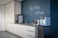 a kitchen with white cabinets and blue walls that says but first, coffee on the wall