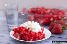 a white plate topped with strawberries next to a bowl of whipped cream and a glass of water