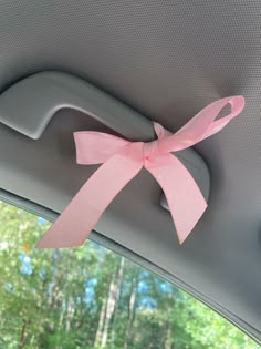 a pink ribbon tied to the side of a car window with trees in the background