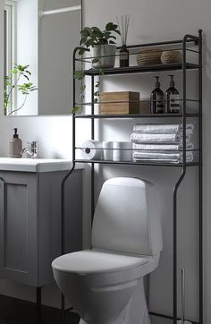 a white toilet sitting next to a sink in a bathroom under a mirror and shelving unit