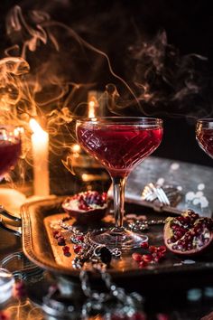 two glasses of pomegranate sit on a tray next to some lit candles