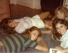 four young women laying on the floor with their cell phones in hand and smiling at the camera