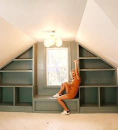 a woman in an orange shirt is sitting on a shelf and reaching up to the sky