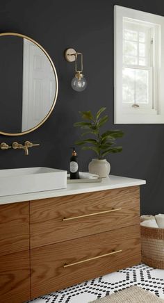 a bathroom with black walls and white counter tops, gold accents and a round mirror on the wall