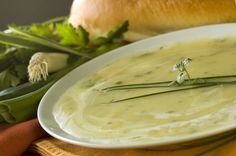 a white bowl filled with soup next to bread and green vegetables on a yellow cloth