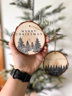 a person holding up a wooden ornament in front of a christmas tree with the words merry christmas written on it