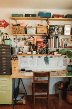 a desk with lots of clutter on it in front of a wall mounted bookcase