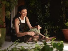 a woman sitting on the floor with potted plants in front of her and smiling