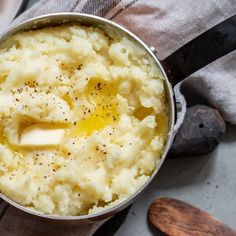 mashed potatoes with butter and seasoning in a pot on a towel next to two wooden spoons