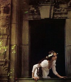 a woman in white dress sitting on the ledge of an old building with her hands behind her head