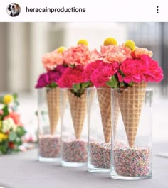 three ice cream cones filled with sprinkles and flowers in vases on a table