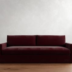 a red couch sitting on top of a hard wood floor next to a white wall