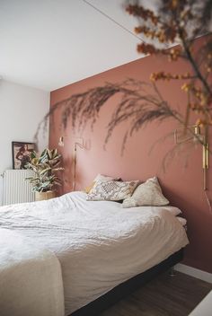 a bed with white sheets and pillows in front of a pink wall that has plants on it