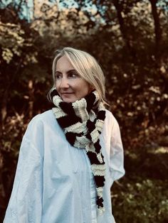 a woman wearing a black and white knitted scarf standing in front of some trees