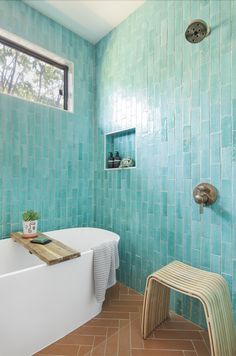 a white bath tub sitting under a window next to a wooden bench in a bathroom