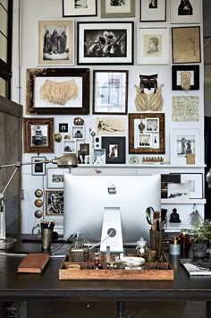 a desk with a computer and lots of pictures on the wall