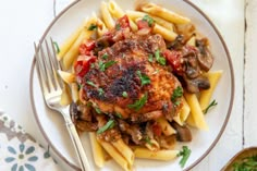 a white plate topped with pasta and meat covered in sauce, garnished with parsley