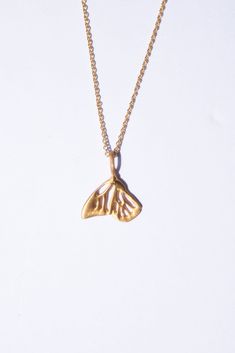 a gold necklace with a small yellow butterfly on it's back end, sitting on a white surface