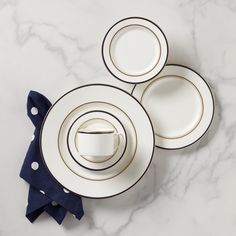 three white and gold dinnerware on a marble countertop with blue napkins next to it