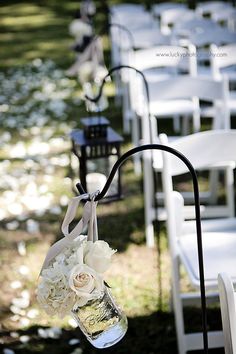 an image of a wedding set up with white chairs and flowers in vases on the aisle