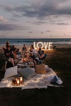 a group of people sitting around a table on top of a field next to the ocean