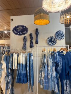 several blue and white shirts hanging on racks in a clothing store with lights above them