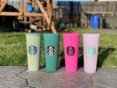 three different colored starbucks cups sitting on the ground