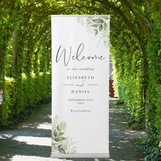 a welcome sign in the middle of a path with greenery on either side and an archway at the end