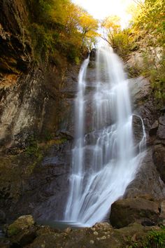 there is a waterfall in the middle of some rocks and trees with leaves around it