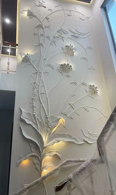 a white wall with flowers and leaves on it in the middle of a room next to a window