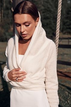 a woman wearing a white robe standing in front of a tree and holding her hands together