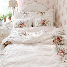 a white bed with pink flowers on it in a room next to a lamp and window