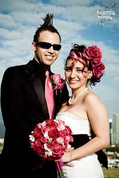 a bride and groom pose for a photo in front of the city skyline with their pink bouquet