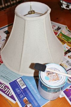 a lamp shade sitting on top of a table next to magazines and a paintbrush