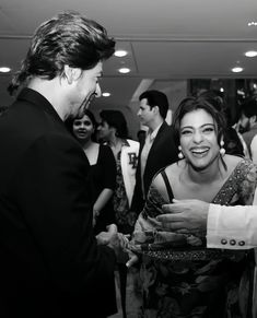 a man in a suit talking to a woman at a party with other people standing around